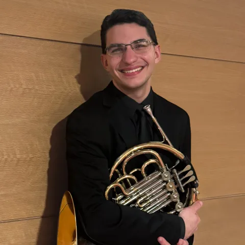 Chris Giannaras smiling and holding his french horn.