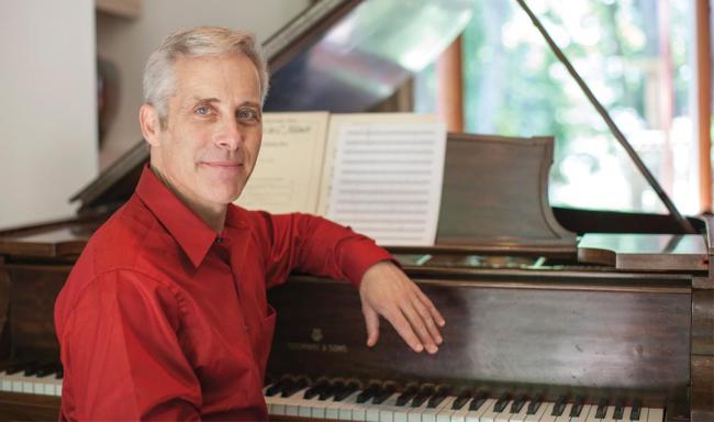 Steven Sametz sitting down, resting his arm on a piano.