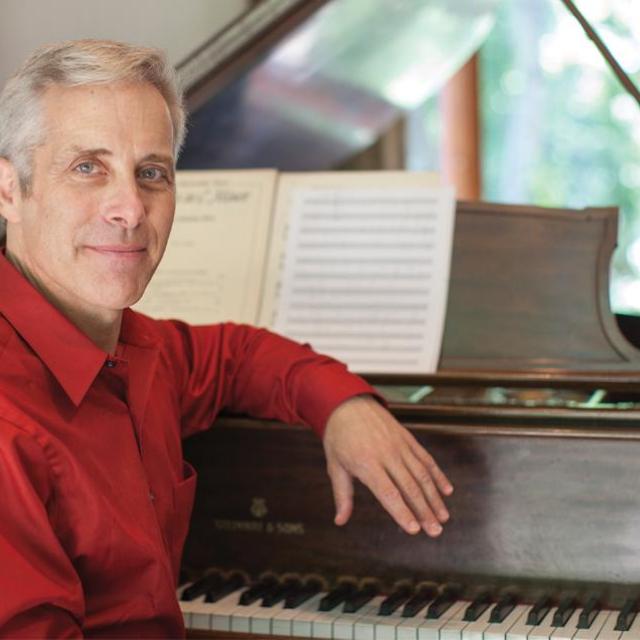 Steven Sametz sitting down, resting his arm on a piano.