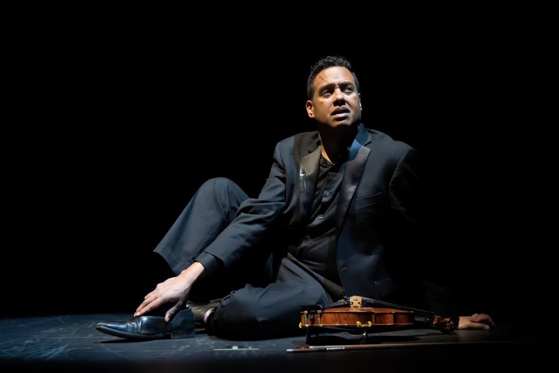 Michael Jorgensen sitting on the stage looking up with his violin next to him.