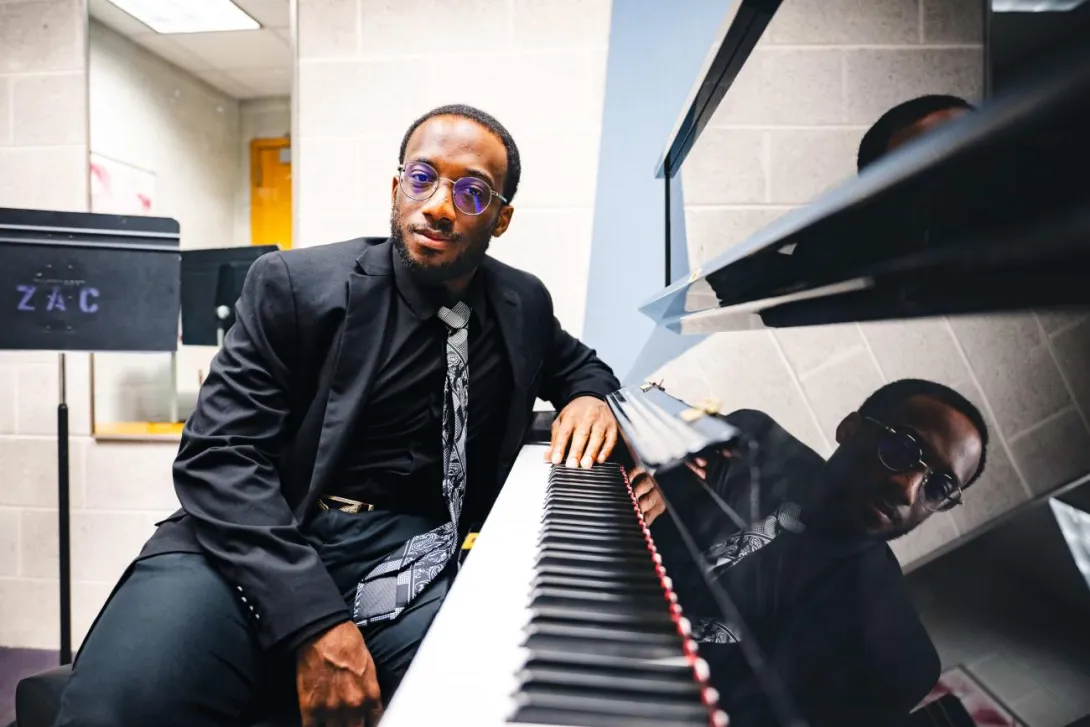 Loba Salami sits at a piano wearing a black suit and tie.